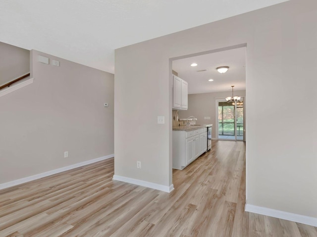 kitchen with pendant lighting, sink, white cabinets, a notable chandelier, and light hardwood / wood-style floors