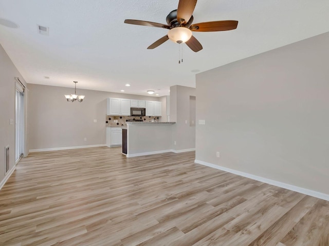 unfurnished living room featuring ceiling fan with notable chandelier and light wood-type flooring