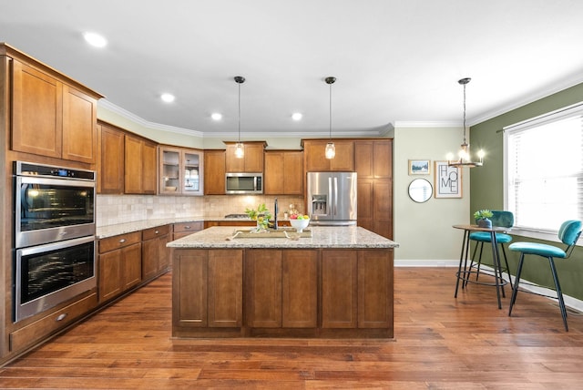 kitchen featuring appliances with stainless steel finishes, pendant lighting, an island with sink, backsplash, and light stone counters