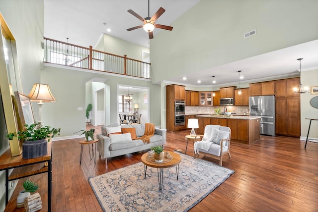 living room featuring a high ceiling, ornamental molding, dark hardwood / wood-style floors, and ceiling fan with notable chandelier