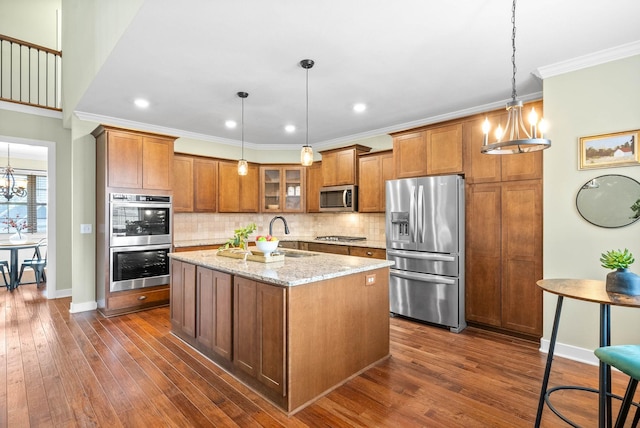 kitchen with appliances with stainless steel finishes, decorative light fixtures, light stone countertops, and a kitchen island