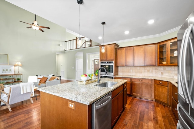 kitchen with pendant lighting, an island with sink, sink, light stone counters, and stainless steel appliances