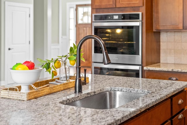 kitchen with double oven, decorative backsplash, light stone countertops, and sink