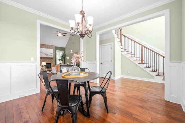 dining area with wood-type flooring, vaulted ceiling, crown molding, and a fireplace