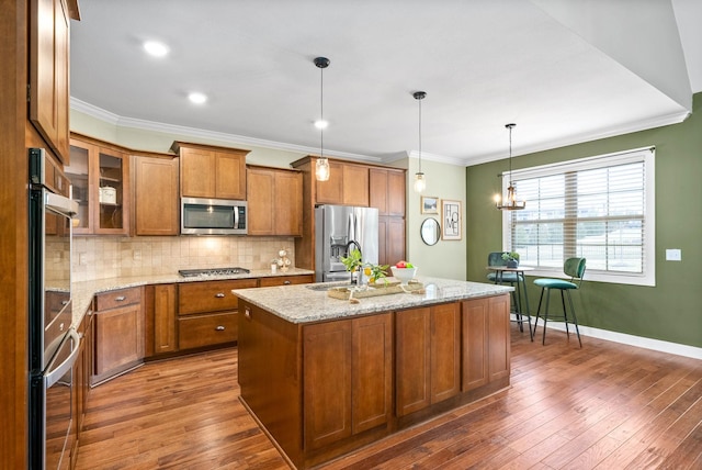 kitchen featuring appliances with stainless steel finishes, dark hardwood / wood-style floors, pendant lighting, light stone countertops, and a kitchen island with sink