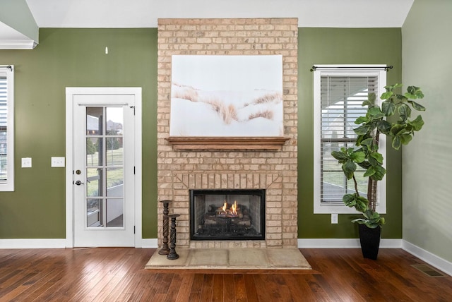 unfurnished living room with dark wood-type flooring, a brick fireplace, and a wealth of natural light