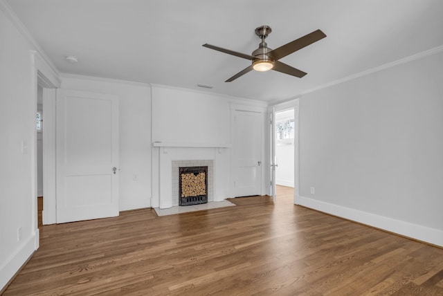 unfurnished living room featuring wood-type flooring, ornamental molding, a tile fireplace, and ceiling fan