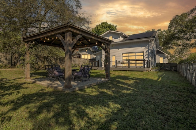 back house at dusk featuring a gazebo, a patio area, and a lawn