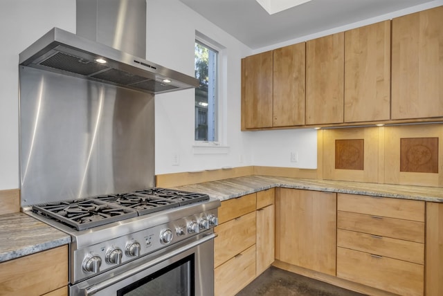 kitchen with stainless steel gas range, light stone counters, and wall chimney exhaust hood