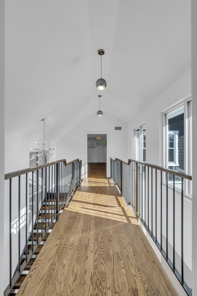 hallway with lofted ceiling, hardwood / wood-style floors, and a notable chandelier