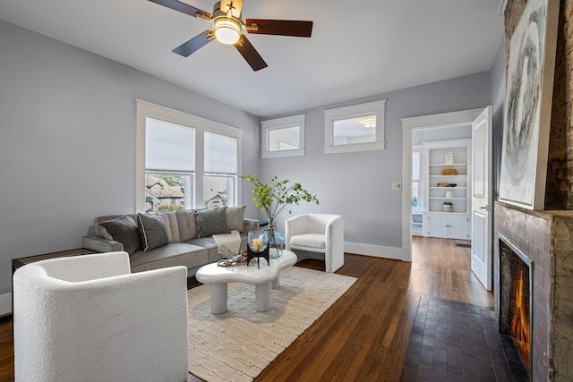 living room featuring built in features, a tile fireplace, dark hardwood / wood-style floors, and ceiling fan