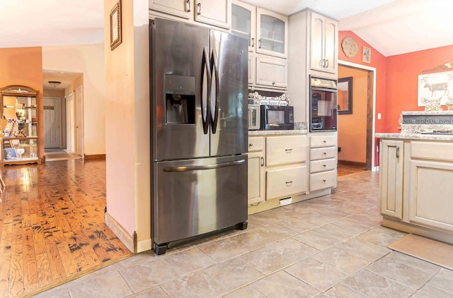 kitchen with cream cabinetry, light stone countertops, vaulted ceiling, and black appliances