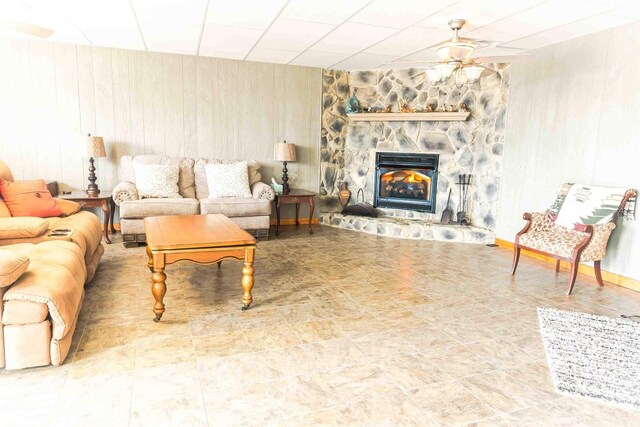 living room featuring a stone fireplace, ceiling fan, and wood walls