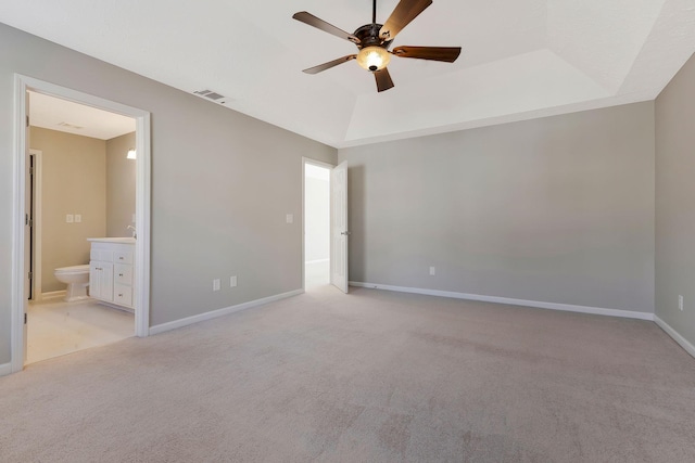 unfurnished bedroom featuring ensuite bathroom, light colored carpet, ceiling fan, and a tray ceiling