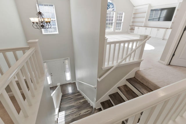 stairway with hardwood / wood-style floors, a towering ceiling, a wealth of natural light, and a notable chandelier