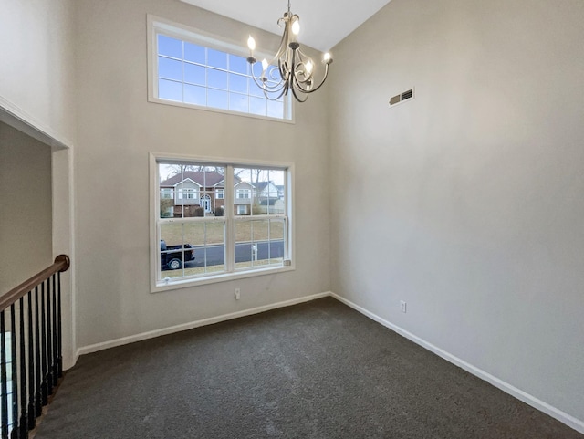 carpeted spare room featuring a towering ceiling and a notable chandelier