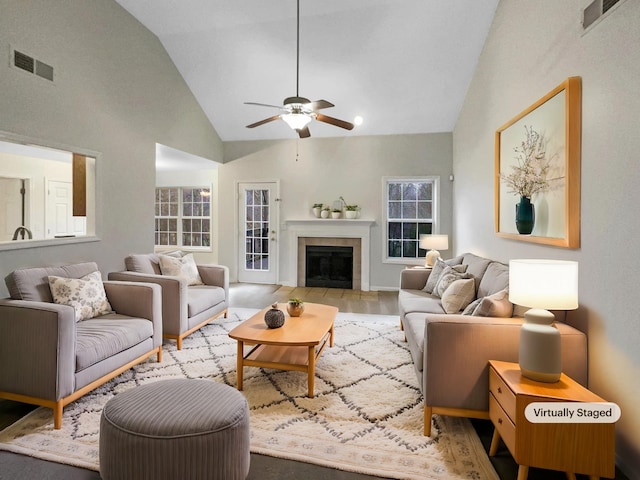 living room featuring a tiled fireplace, high vaulted ceiling, ceiling fan, and light hardwood / wood-style floors