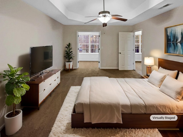 carpeted bedroom with a raised ceiling and ceiling fan