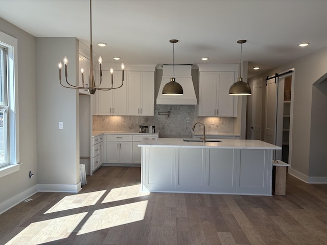 kitchen featuring custom exhaust hood, light countertops, decorative backsplash, a barn door, and a sink