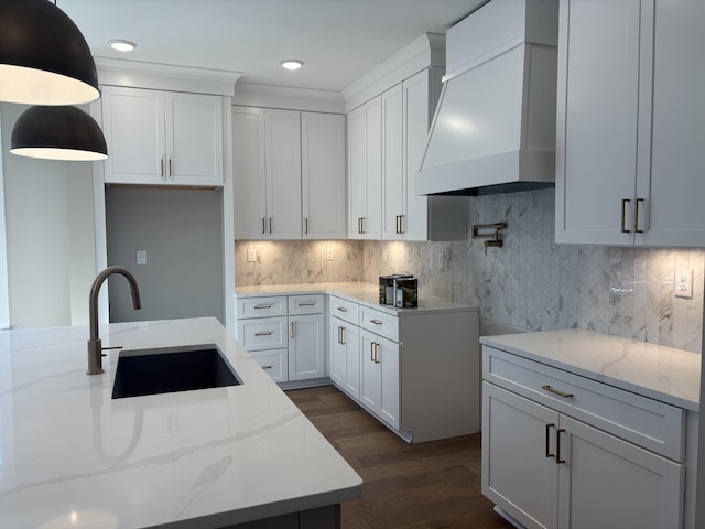 kitchen with dark wood-style floors, custom range hood, a sink, light stone countertops, and backsplash