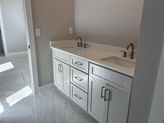 full bathroom featuring marble finish floor, double vanity, a sink, and baseboards