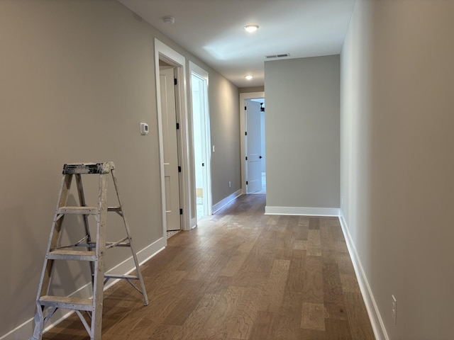 corridor with baseboards, visible vents, and wood finished floors