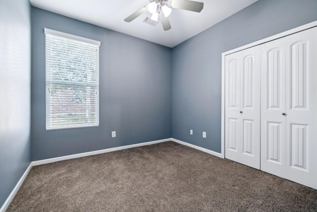 unfurnished bedroom featuring multiple windows, dark colored carpet, ceiling fan, and a closet