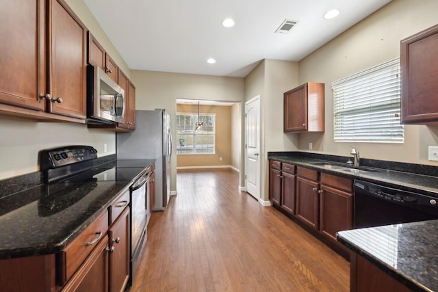 kitchen with sink, dark wood-type flooring, black appliances, and dark stone counters