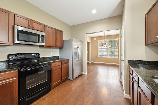 kitchen featuring dark stone countertops, hanging light fixtures, light wood-type flooring, and appliances with stainless steel finishes