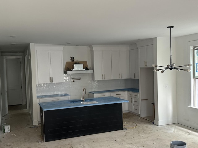 kitchen featuring decorative backsplash, white cabinets, a sink, and a center island with sink