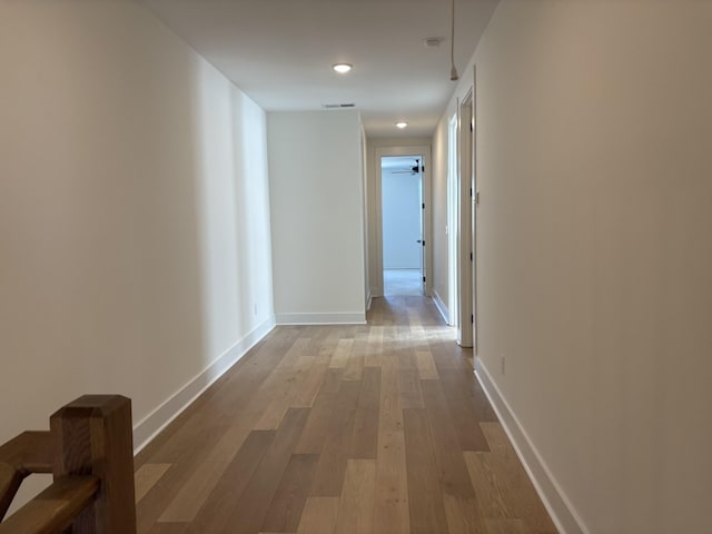 hallway with wood finished floors, visible vents, and baseboards