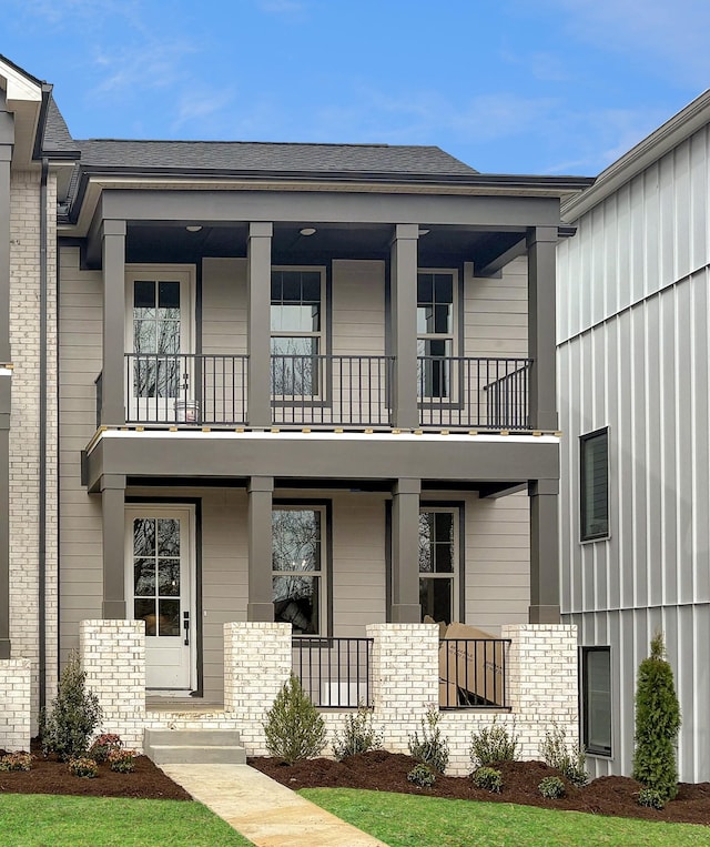 townhome / multi-family property featuring covered porch, brick siding, a balcony, and roof with shingles