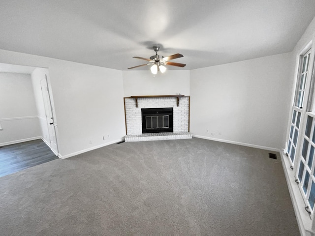 unfurnished living room with ceiling fan, dark carpet, and a brick fireplace