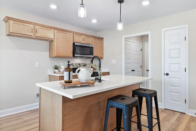 kitchen with pendant lighting, a center island with sink, light brown cabinetry, and light hardwood / wood-style flooring