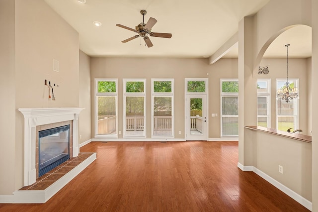 unfurnished living room featuring ceiling fan, hardwood / wood-style flooring, a tile fireplace, and a healthy amount of sunlight