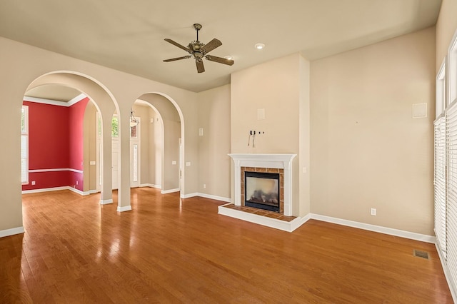 unfurnished living room with a tiled fireplace, hardwood / wood-style flooring, and ceiling fan