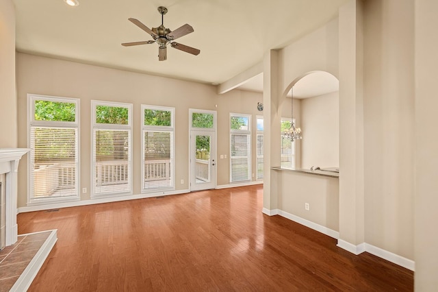 unfurnished living room with ceiling fan with notable chandelier, a fireplace, and wood-type flooring