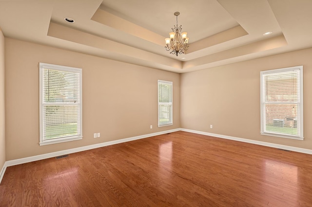 empty room with hardwood / wood-style flooring, a raised ceiling, and an inviting chandelier