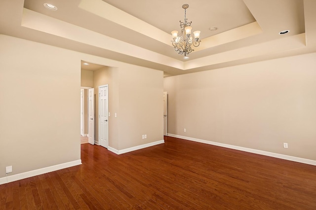 unfurnished room with dark hardwood / wood-style floors, a raised ceiling, and a chandelier