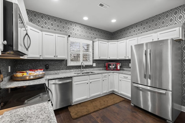 kitchen with stainless steel appliances, white cabinetry, sink, and light stone counters