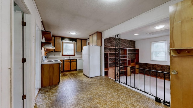 kitchen with sink, white appliances, a textured ceiling, and brick wall