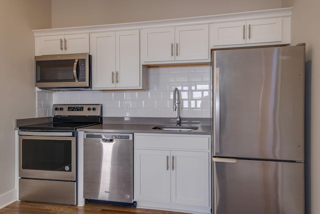 kitchen featuring appliances with stainless steel finishes, sink, white cabinets, dark hardwood / wood-style flooring, and decorative backsplash