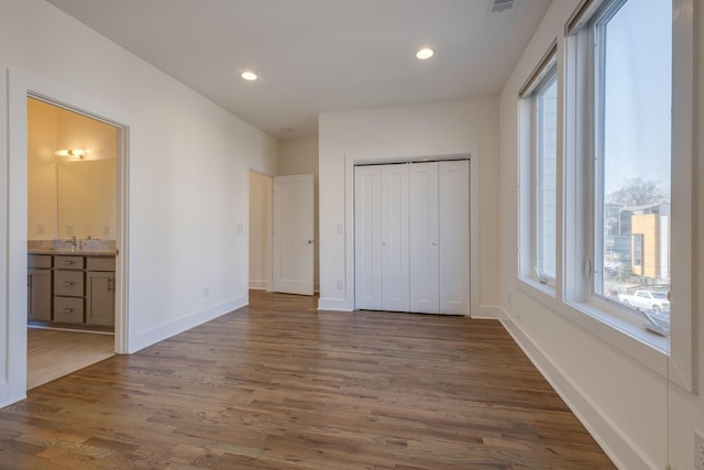 unfurnished bedroom with dark wood-type flooring, ensuite bathroom, sink, and a closet