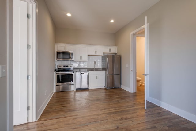 kitchen featuring sink, hardwood / wood-style flooring, appliances with stainless steel finishes, backsplash, and white cabinets