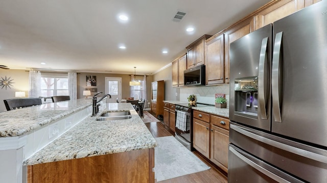 kitchen featuring a spacious island, sink, hanging light fixtures, stainless steel appliances, and light hardwood / wood-style floors