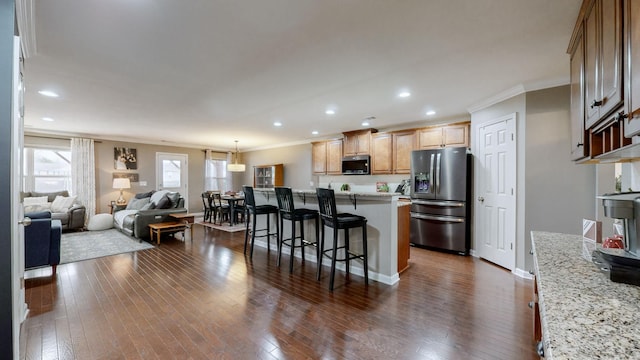 kitchen featuring a kitchen island, appliances with stainless steel finishes, a breakfast bar area, dark hardwood / wood-style flooring, and light stone countertops