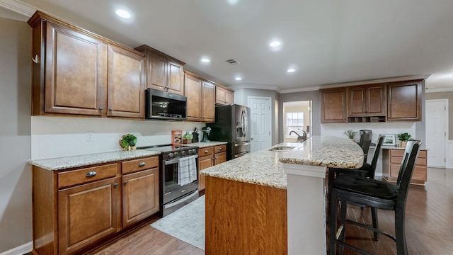 kitchen with appliances with stainless steel finishes, sink, a kitchen bar, light stone countertops, and a center island with sink