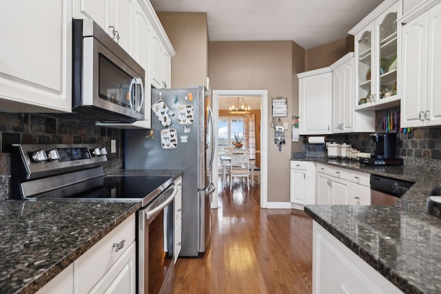 kitchen featuring appliances with stainless steel finishes, white cabinetry, dark hardwood / wood-style flooring, dark stone counters, and decorative backsplash