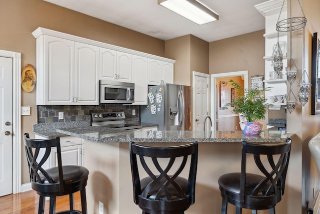 kitchen featuring stainless steel appliances, white cabinetry, dark stone countertops, and a breakfast bar area