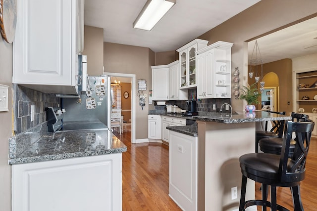 kitchen with a breakfast bar area, white cabinets, range, light hardwood / wood-style floors, and kitchen peninsula